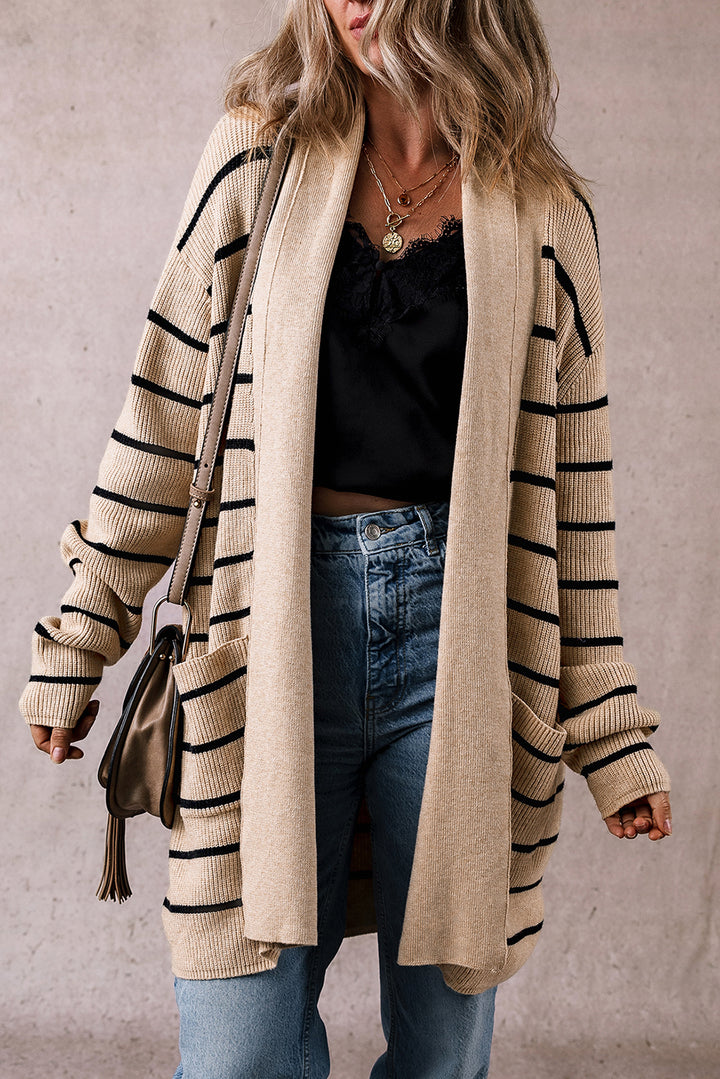 Person wearing a beige cardigan with black stripes, black top, and blue jeans against a neutral background.