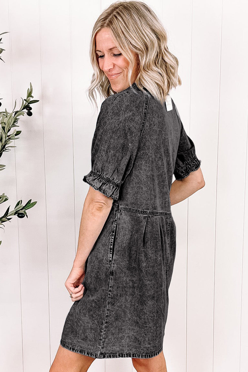Woman wearing a gray denim dress against a white wooden panel background