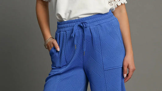 Blue textured wide-leg pants worn by a person on a gray background