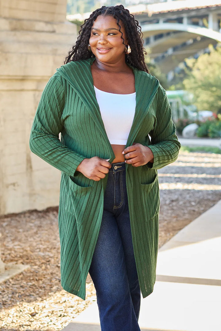 Woman wearing a green cardigan over a white top and blue jeans, standing outdoors.
