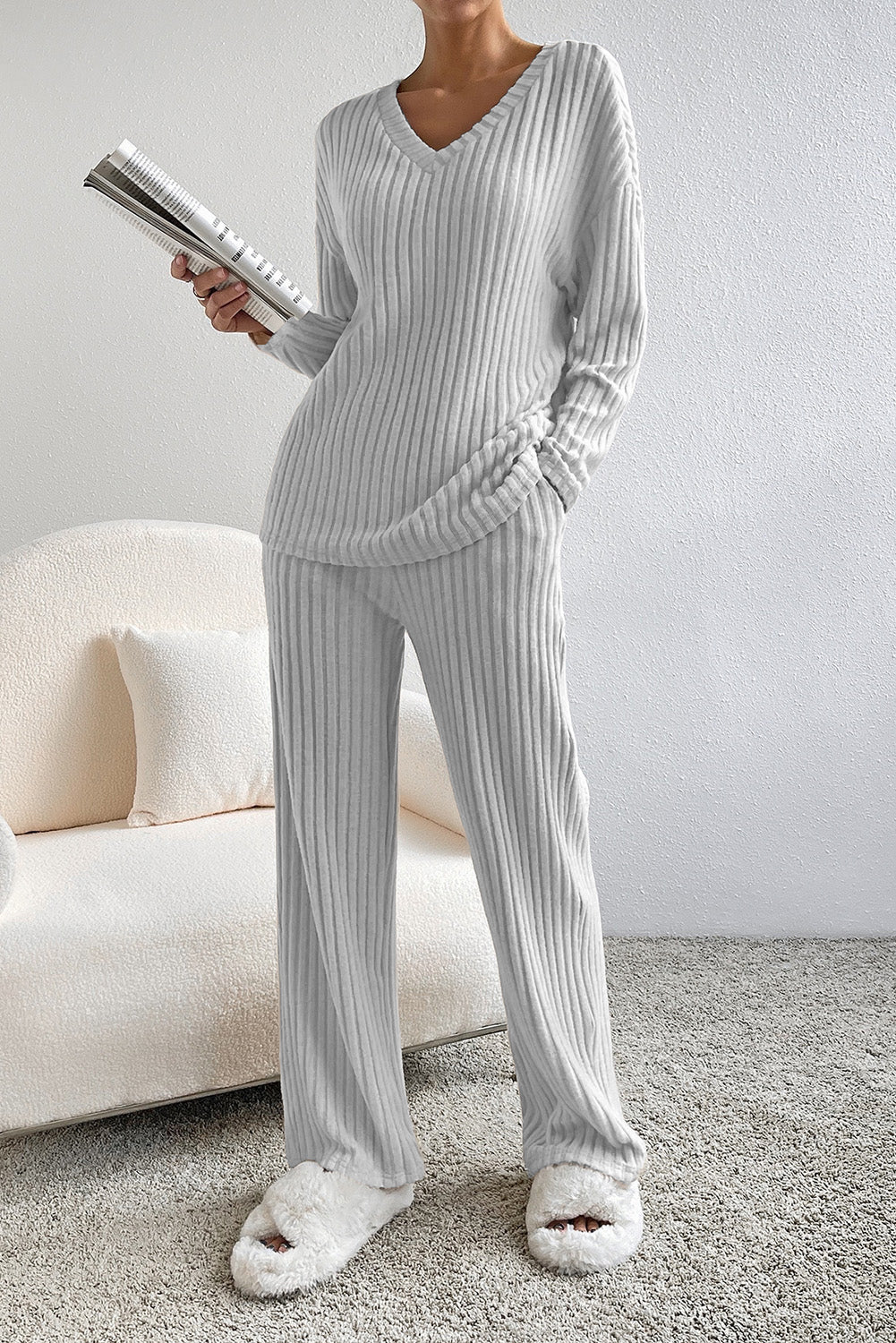 Person wearing gray ribbed pajamas holding a book in a living room.
