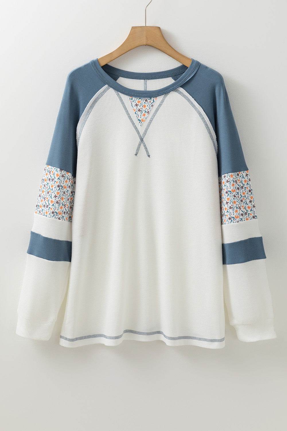 White long-sleeve shirt with blue sleeves and floral cuffs on a hanger against a white background