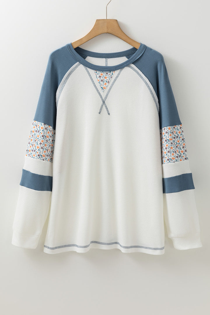 White long-sleeve shirt with blue sleeves and floral cuffs on a hanger against a white background