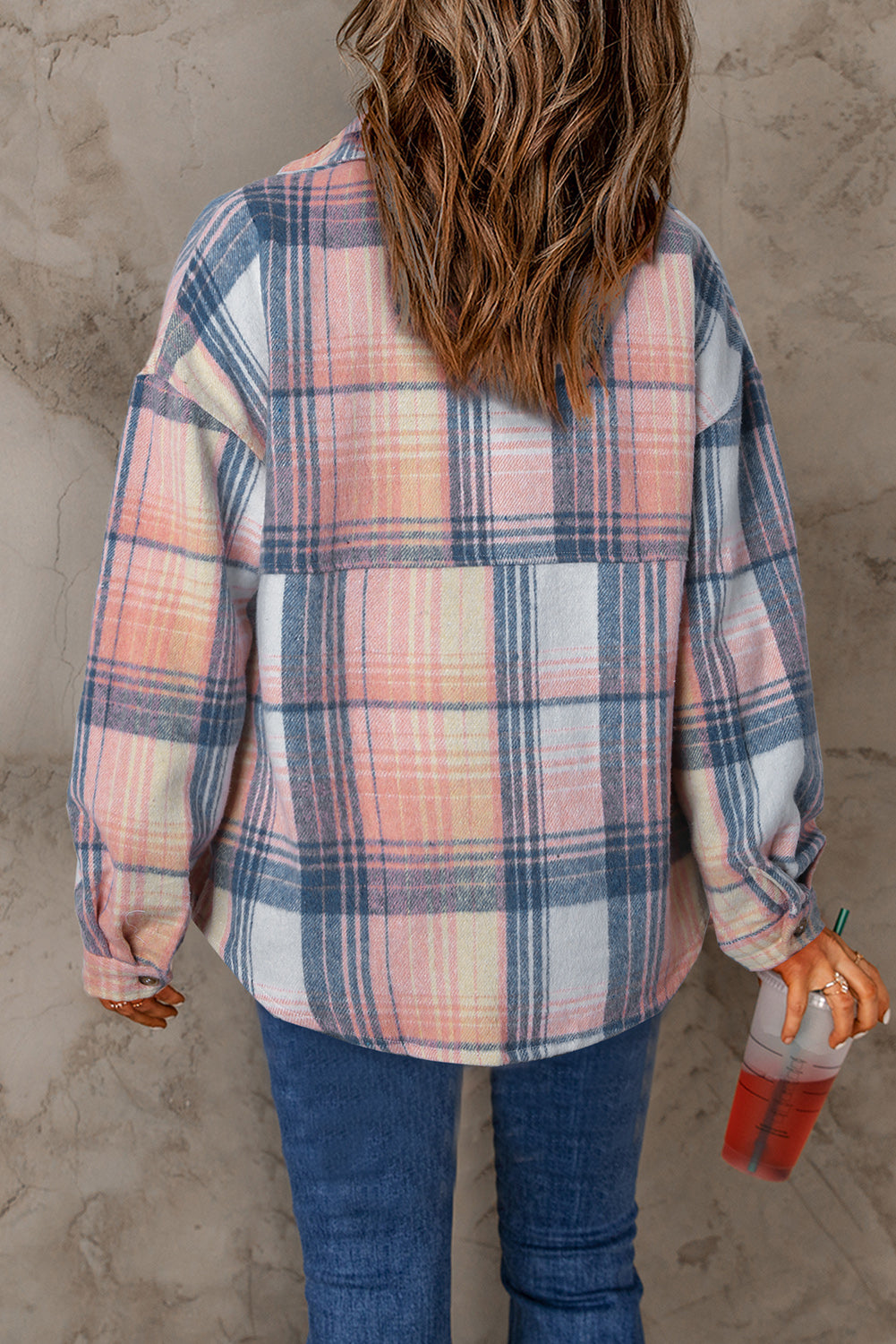Person wearing a plaid shirt and blue jeans against a textured wall.