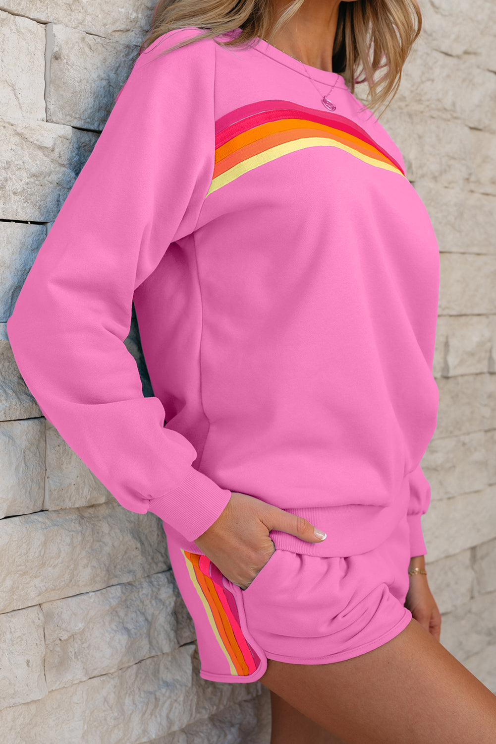 Person wearing a pink outfit with colorful stripes against a stone wall.