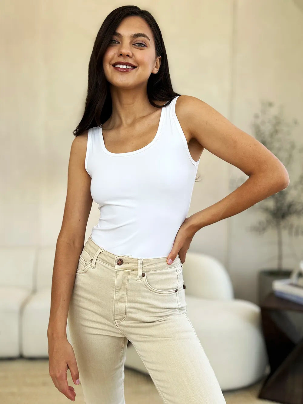 Woman wearing a white tank top and beige pants indoors