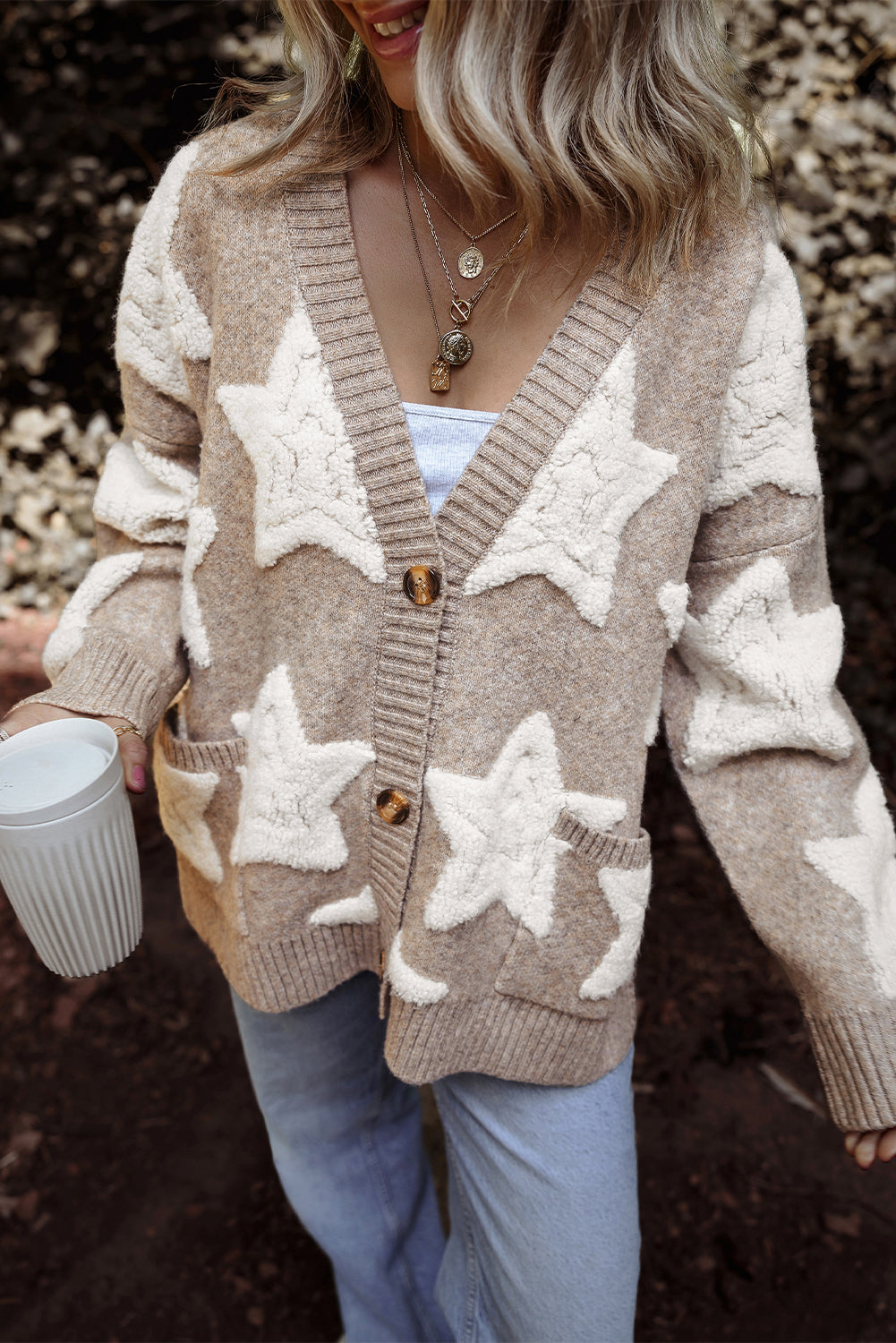 Person wearing a beige cardigan with star patterns, holding a white mug.