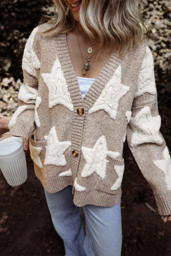 Person wearing a beige cardigan with star patterns, holding a white mug.