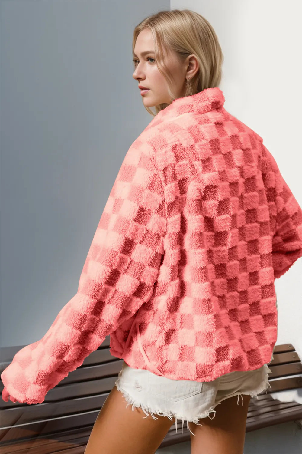 Woman wearing a pink textured jacket and white shorts against a neutral background