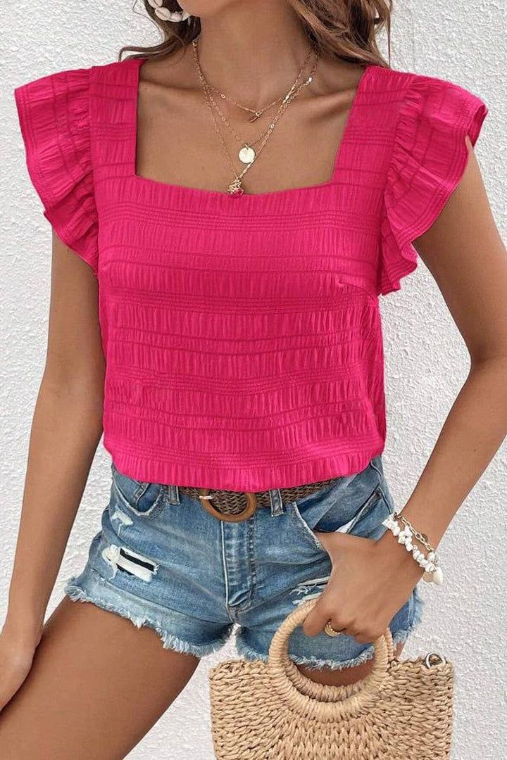 Woman wearing a textured, rose-colored top with ruffled sleeves and square neckline and a pair of jean shorts