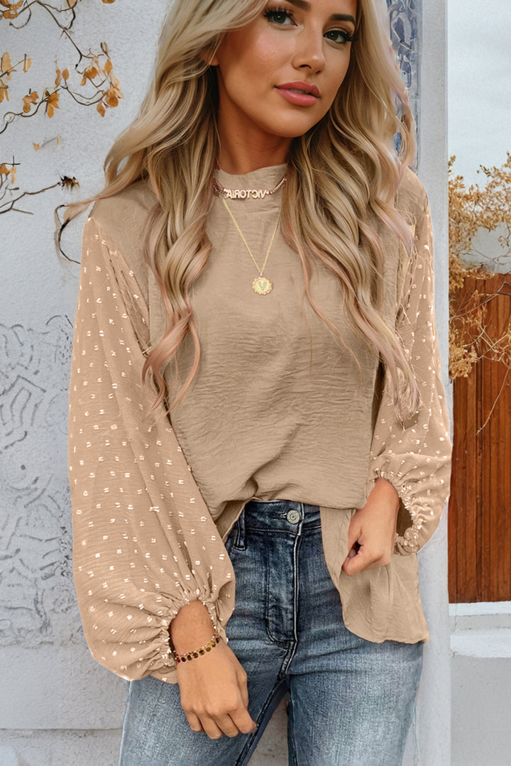 Woman wearing a beige blouse with long sleeves and blue jeans against a decorative wall.