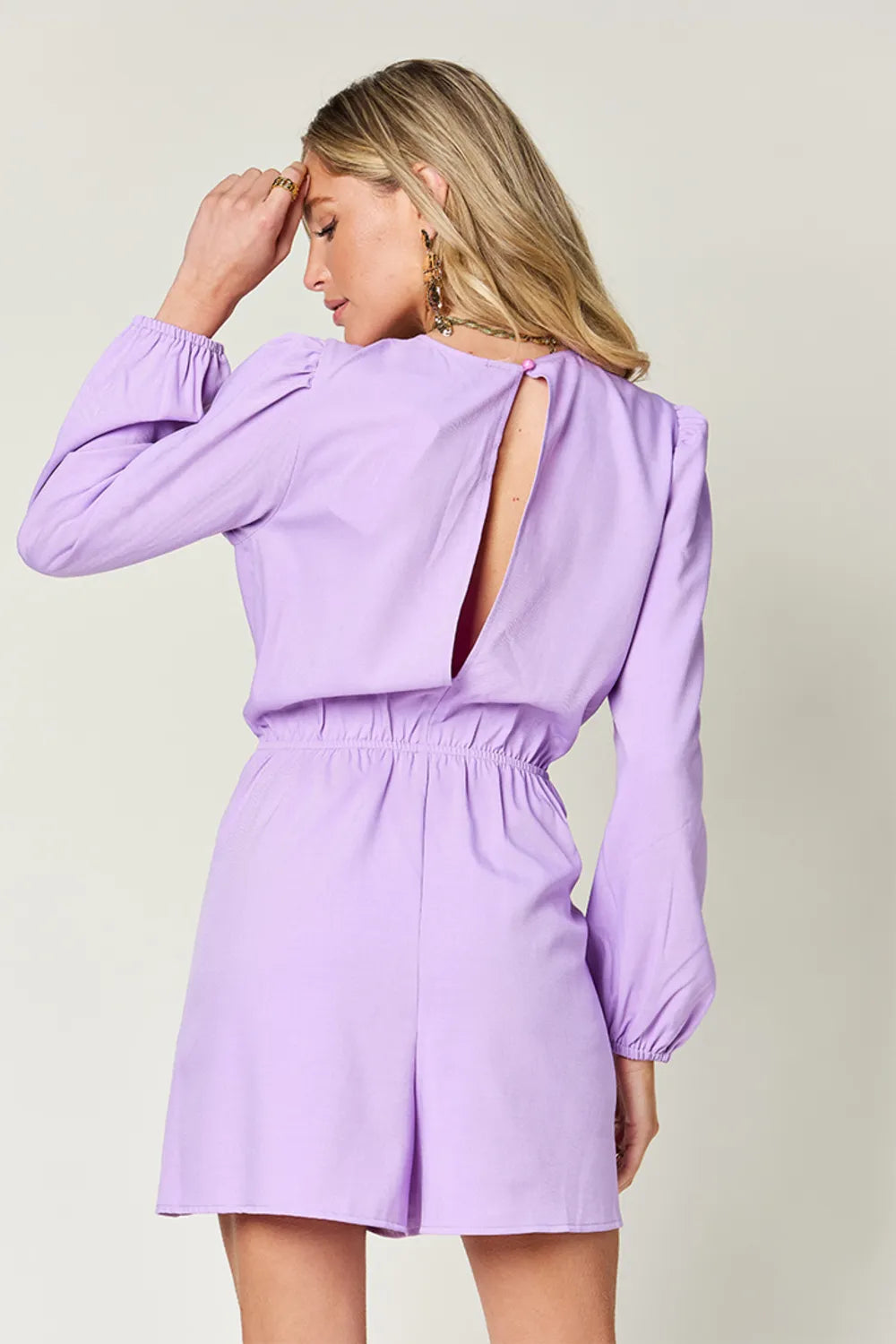 Woman wearing a light purple dress with long sleeves and a cutout back on a plain background