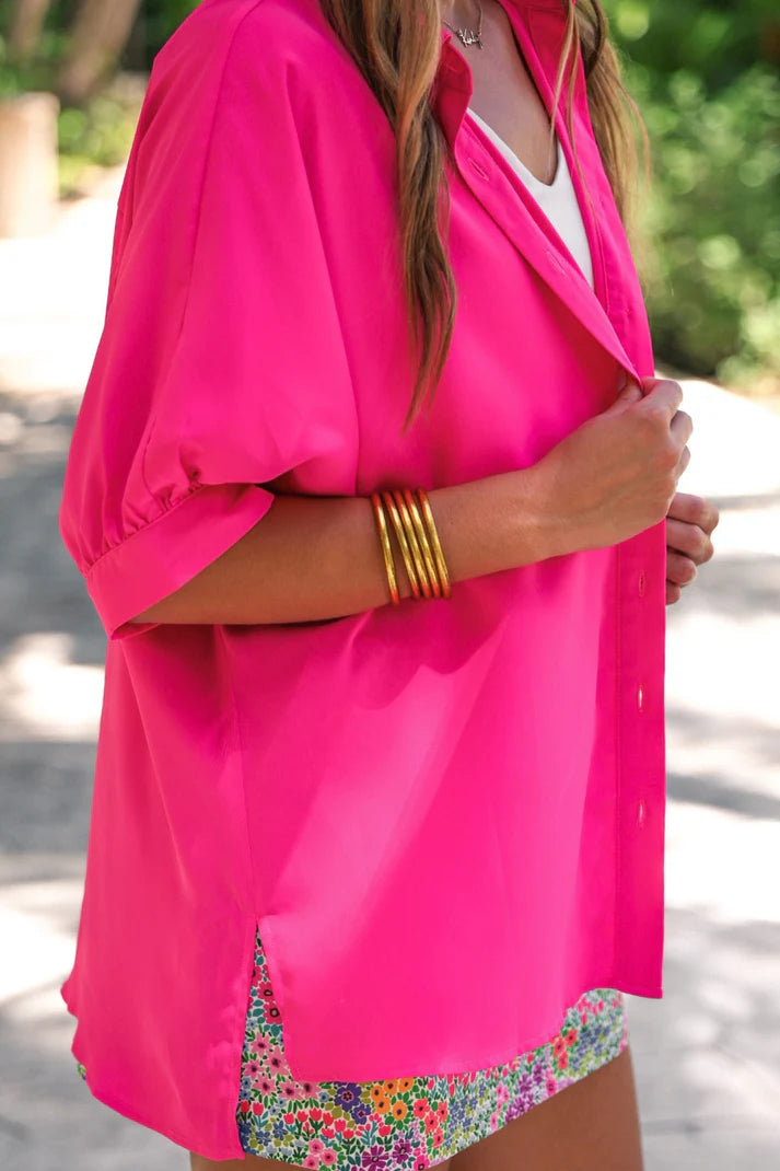 Person wearing a bright pink cover-up over a colorful swimsuit with gold bangles.