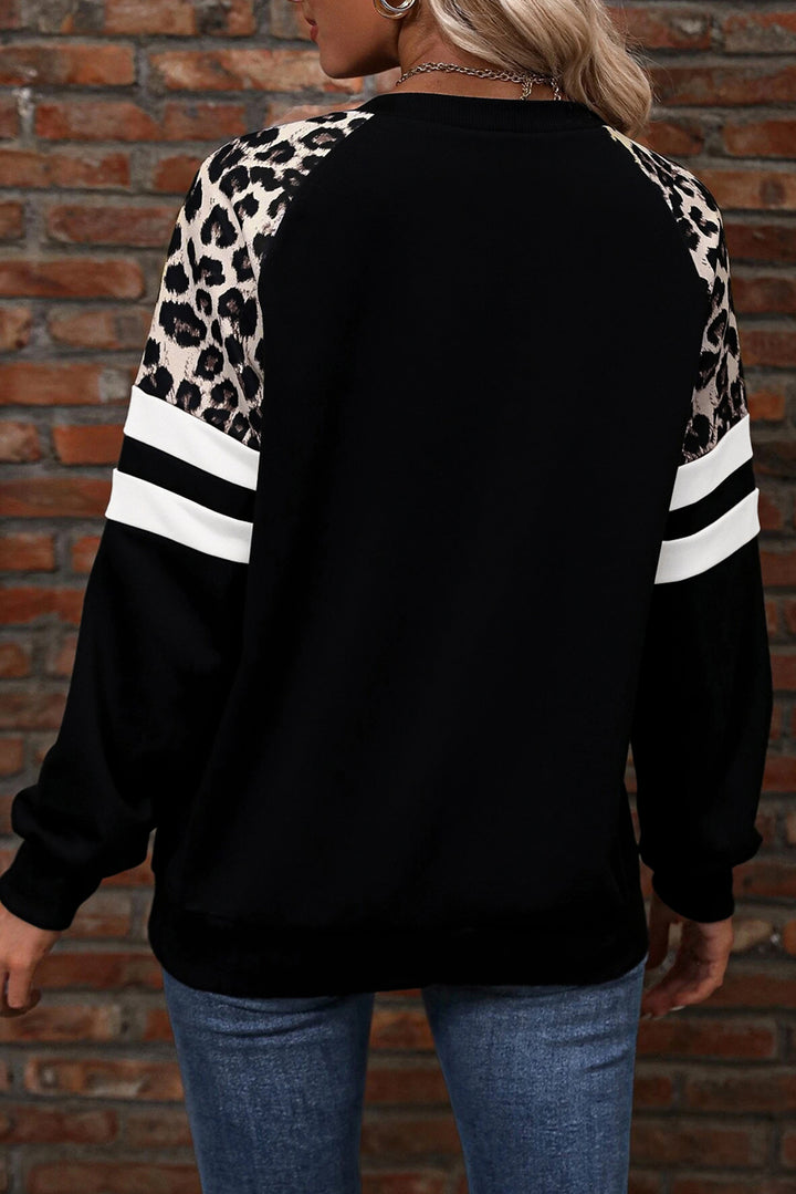 Person wearing a black sweater with leopard print sleeves against a brick wall.