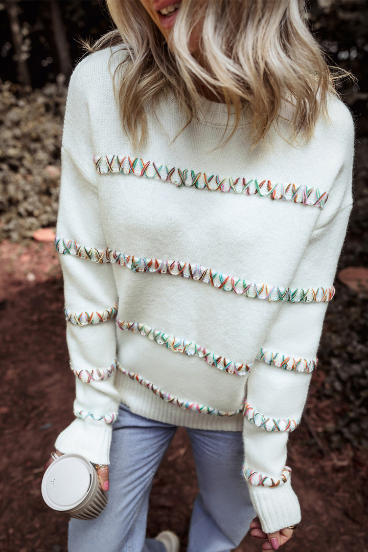 Person wearing a white sweater with decorative trim in an outdoor setting