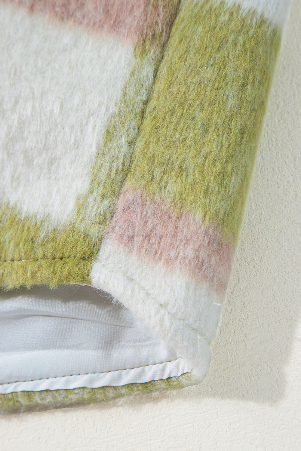 Close-up of a textured fabric with green, pink, and white stripes on a neutral background.