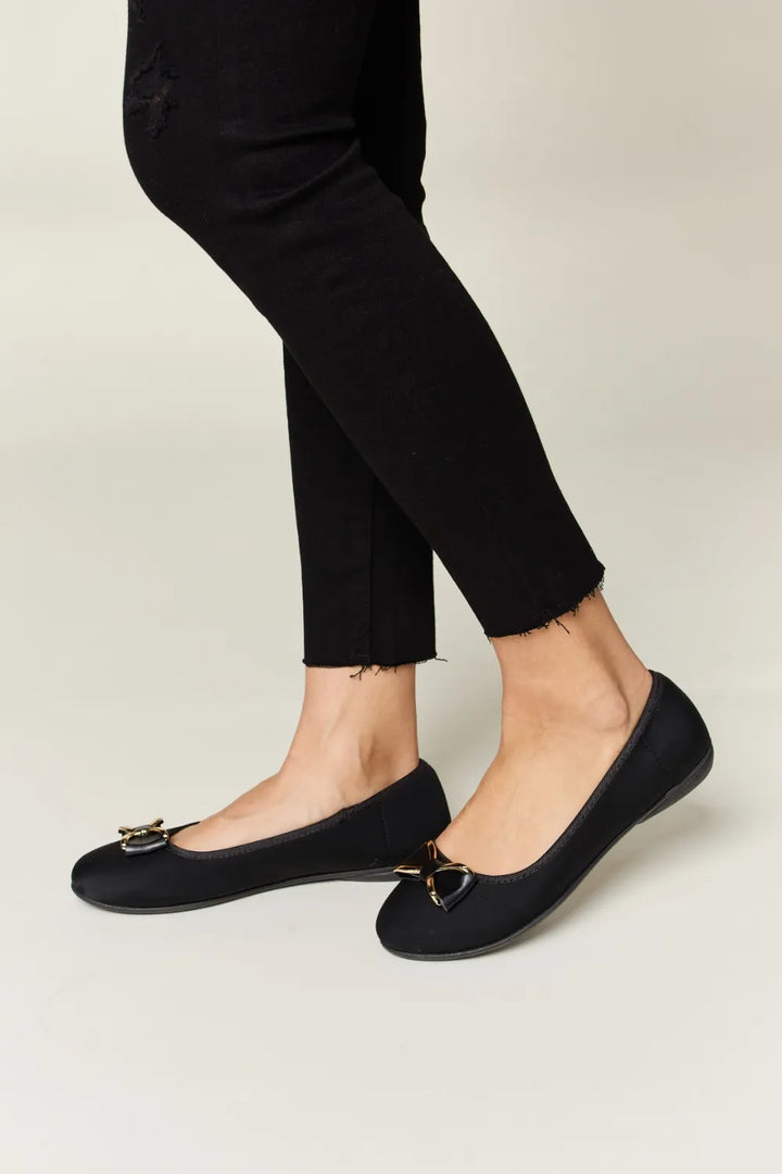Black flats worn with black pants on a light background