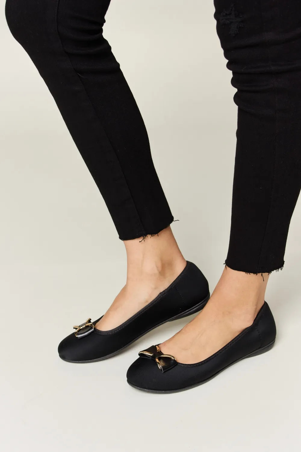 Black flats worn with black pants on a light background