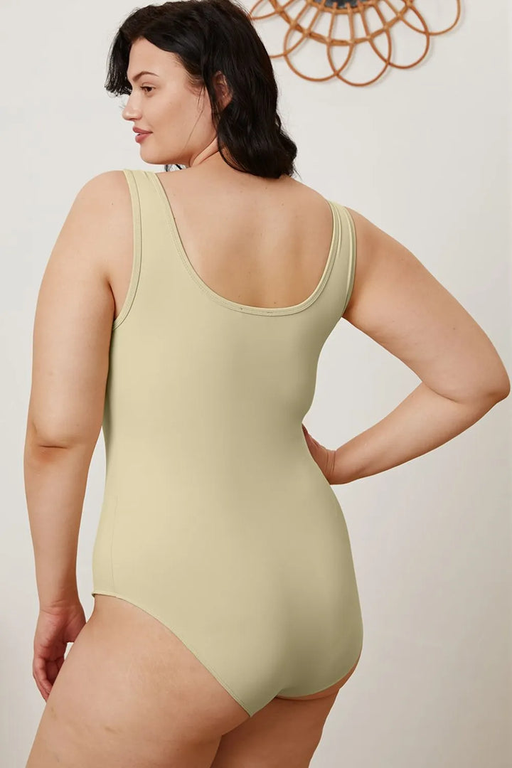 Woman wearing a light green one-piece swimsuit against a plain background