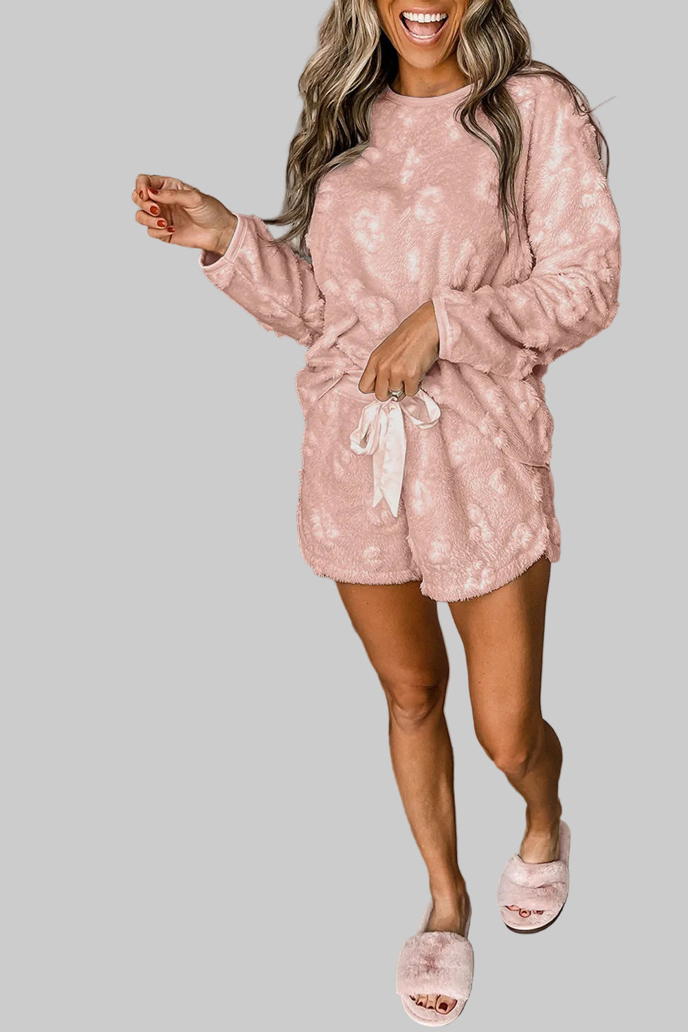 Woman in a pink outfit standing next to a white background.