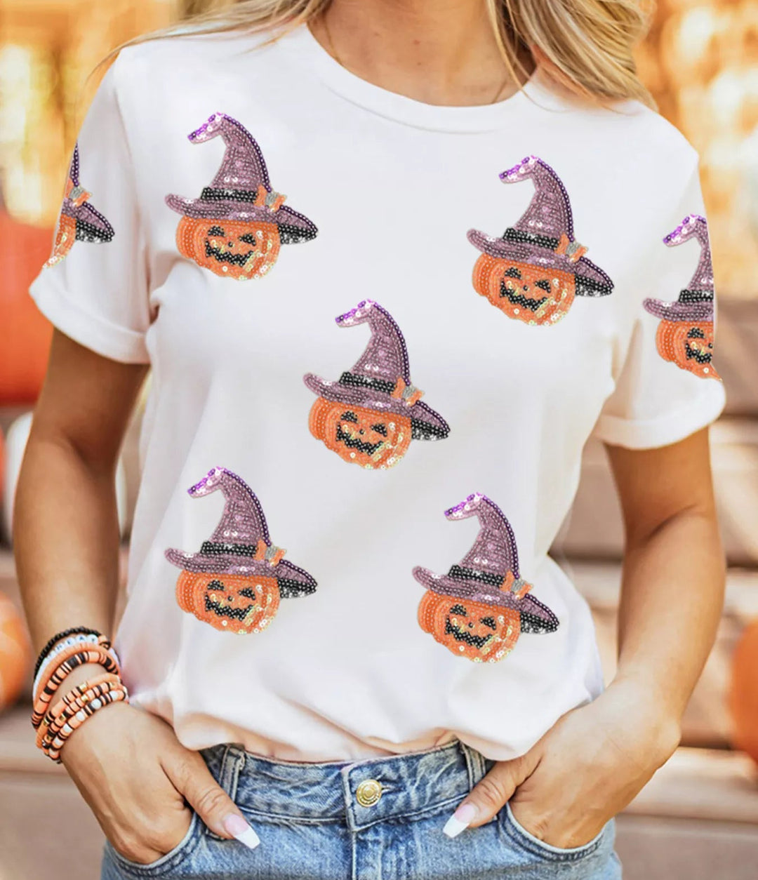 Women wearing white tee shirt with sequence pumpkins wearing a purple sequence hat while hands tucked in jean pockets