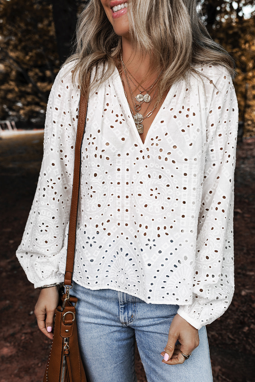 Woman wearing a white blouse with eyelet design and blue jeans, standing outdoors.