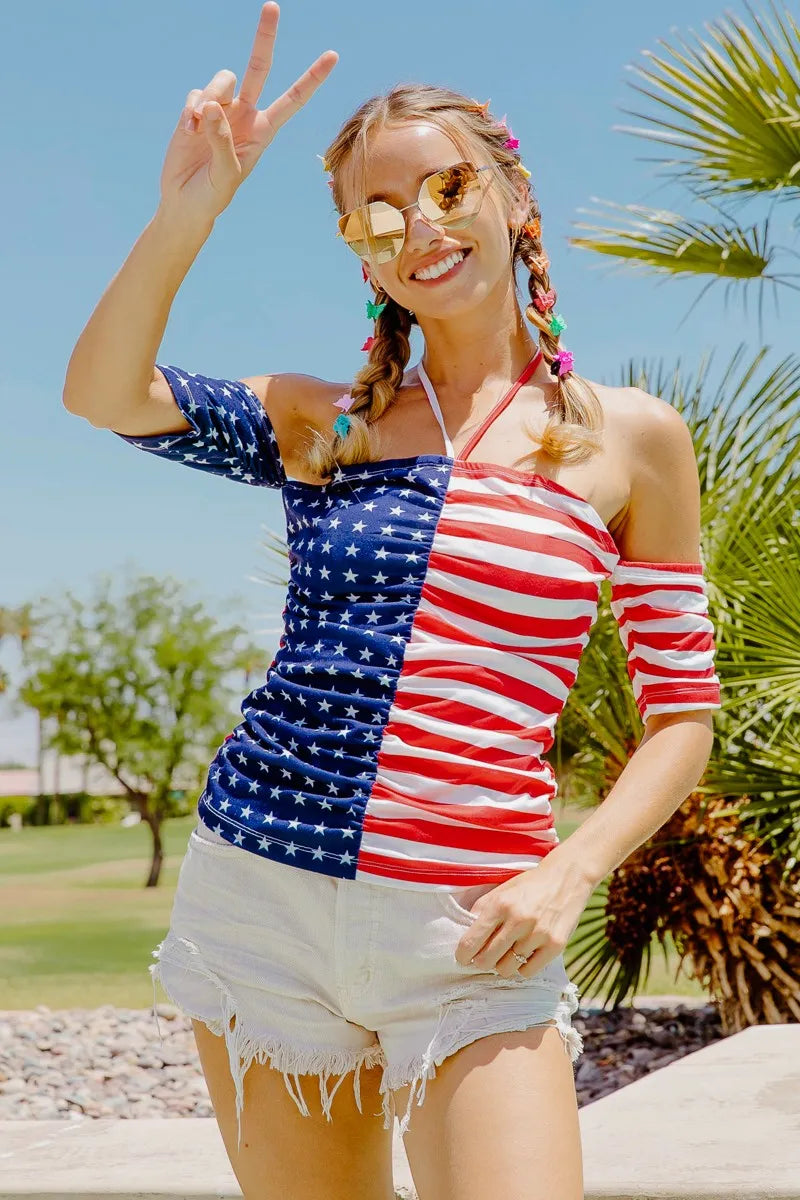 Woman wearing a colorful dress with an American flag design, standing outdoors with palm trees in the background.