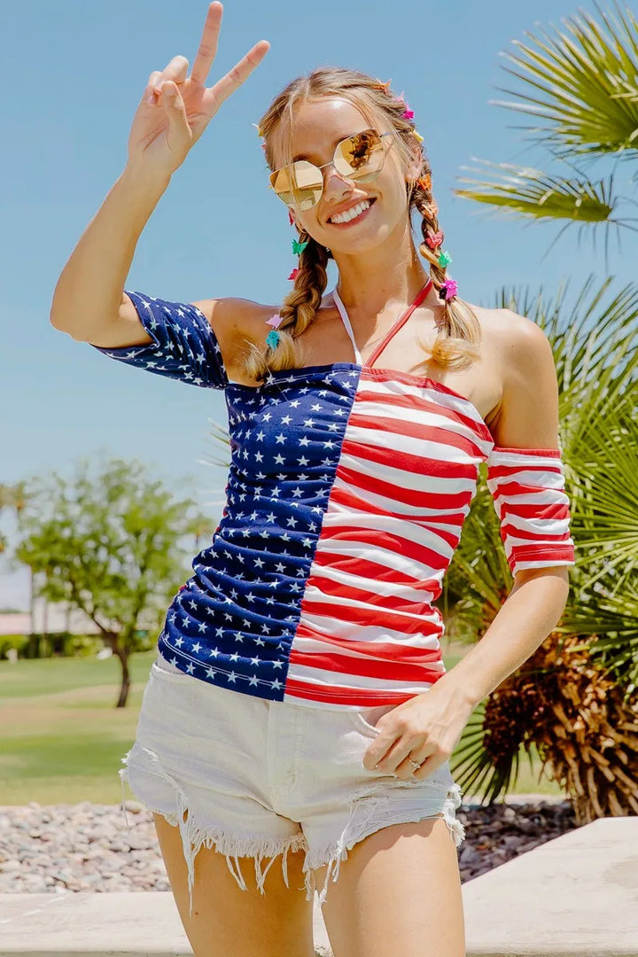 Woman wearing a colorful dress with an American flag design, standing outdoors with palm trees in the background.