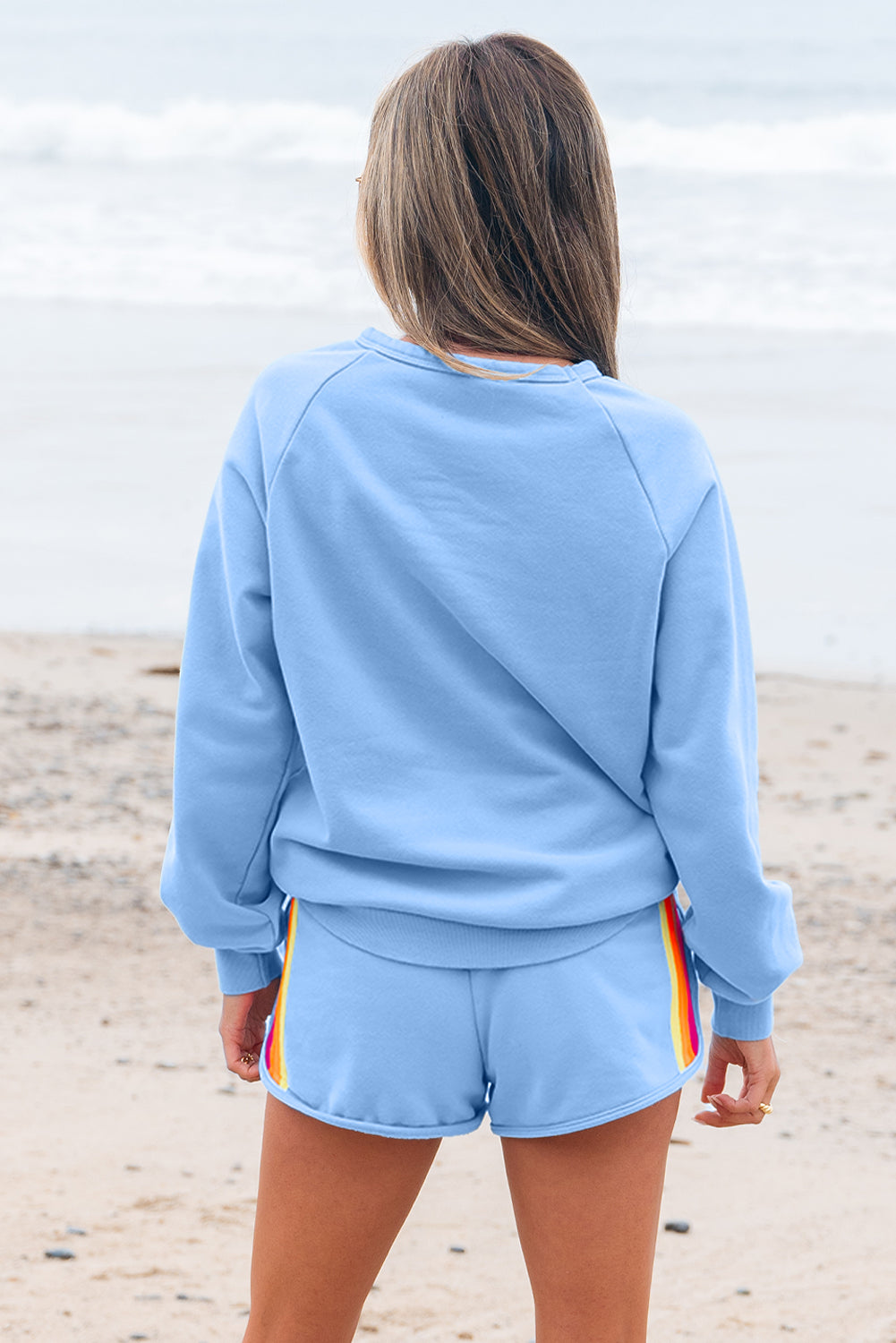 Person wearing a light blue outfit with colorful accents on a beach.