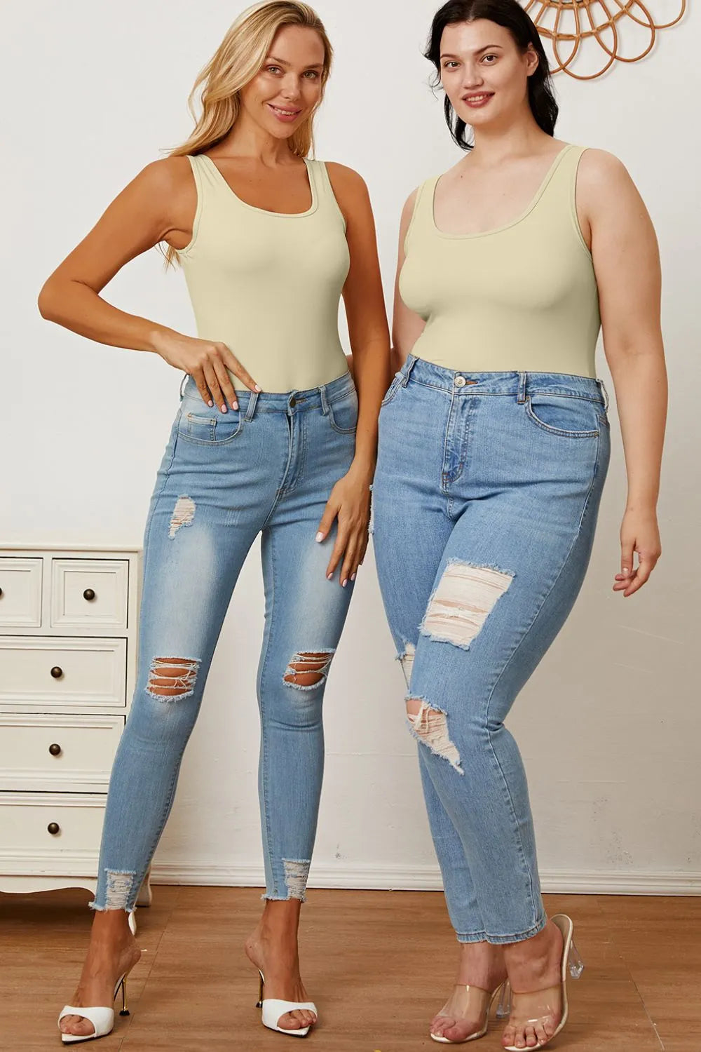 Two women wearing matching light green tank tops and distressed blue jeans in a room.