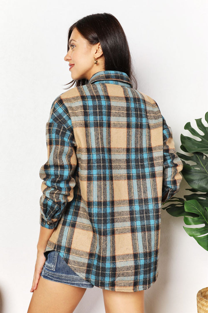 Woman wearing a plaid shirt with a white background and plant to the side