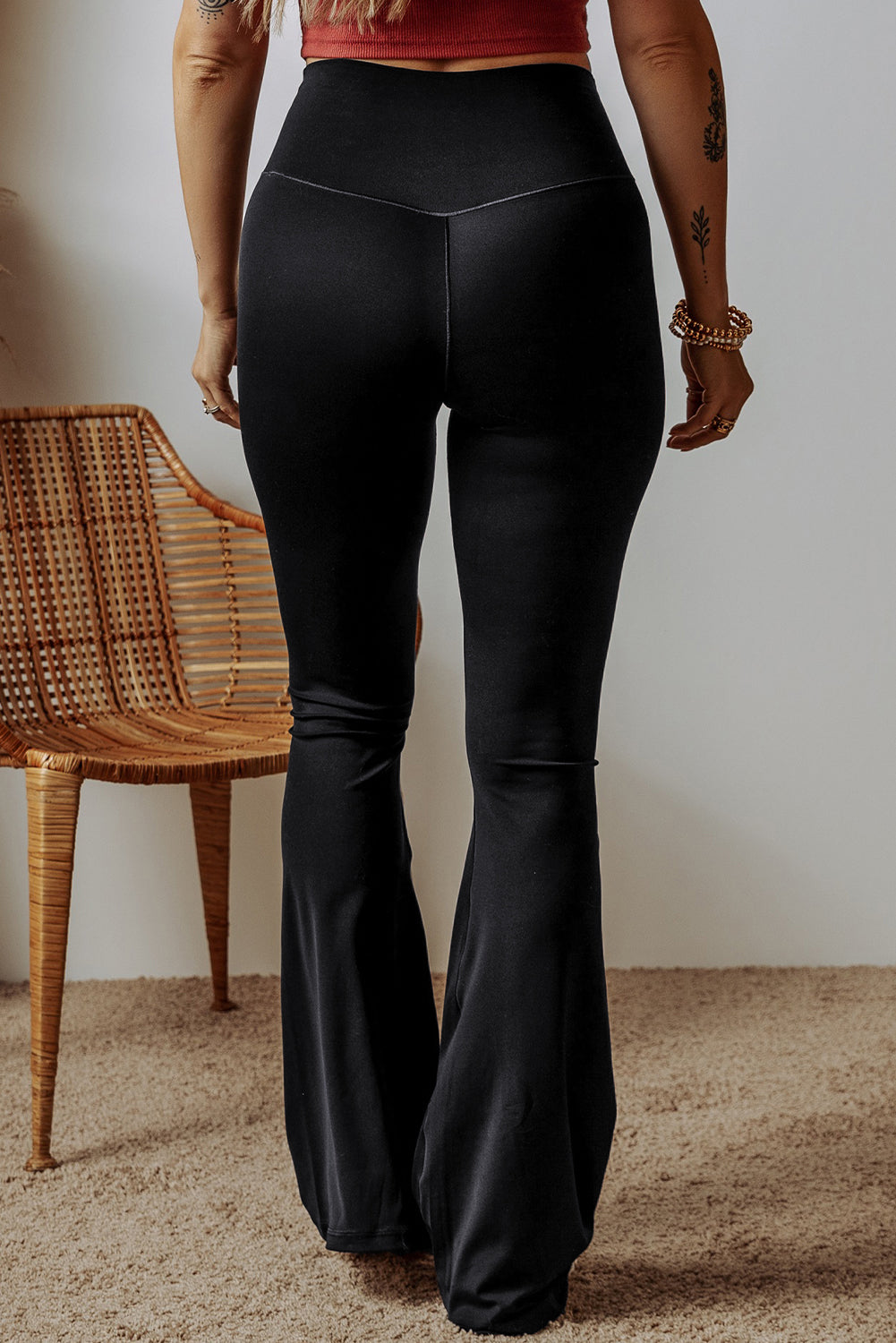 Person wearing black flared pants standing in a room with a wicker chair.