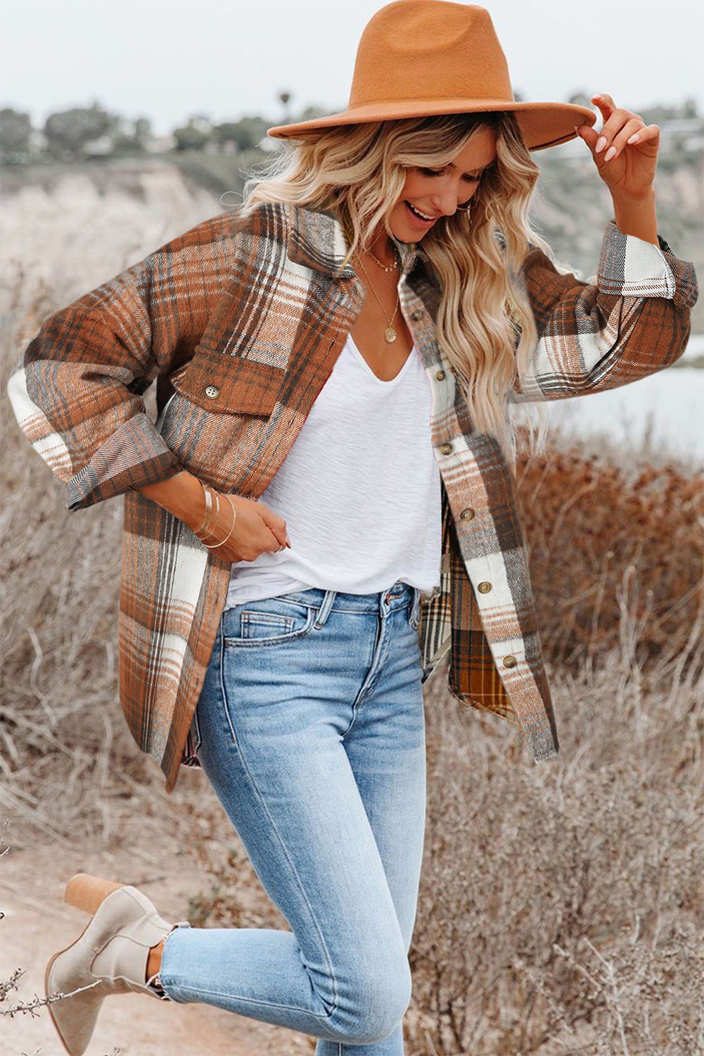 Woman wearing a plaid shirt, white top, jeans, and tan hat in an outdoor setting.