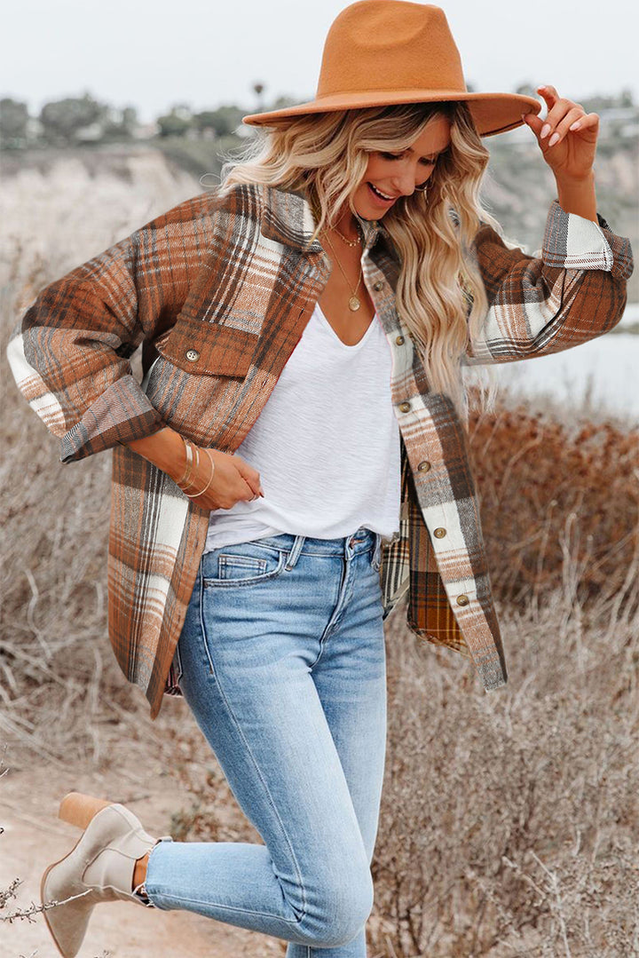 Woman wearing a plaid shirt, white top, jeans, and tan hat in an outdoor setting.