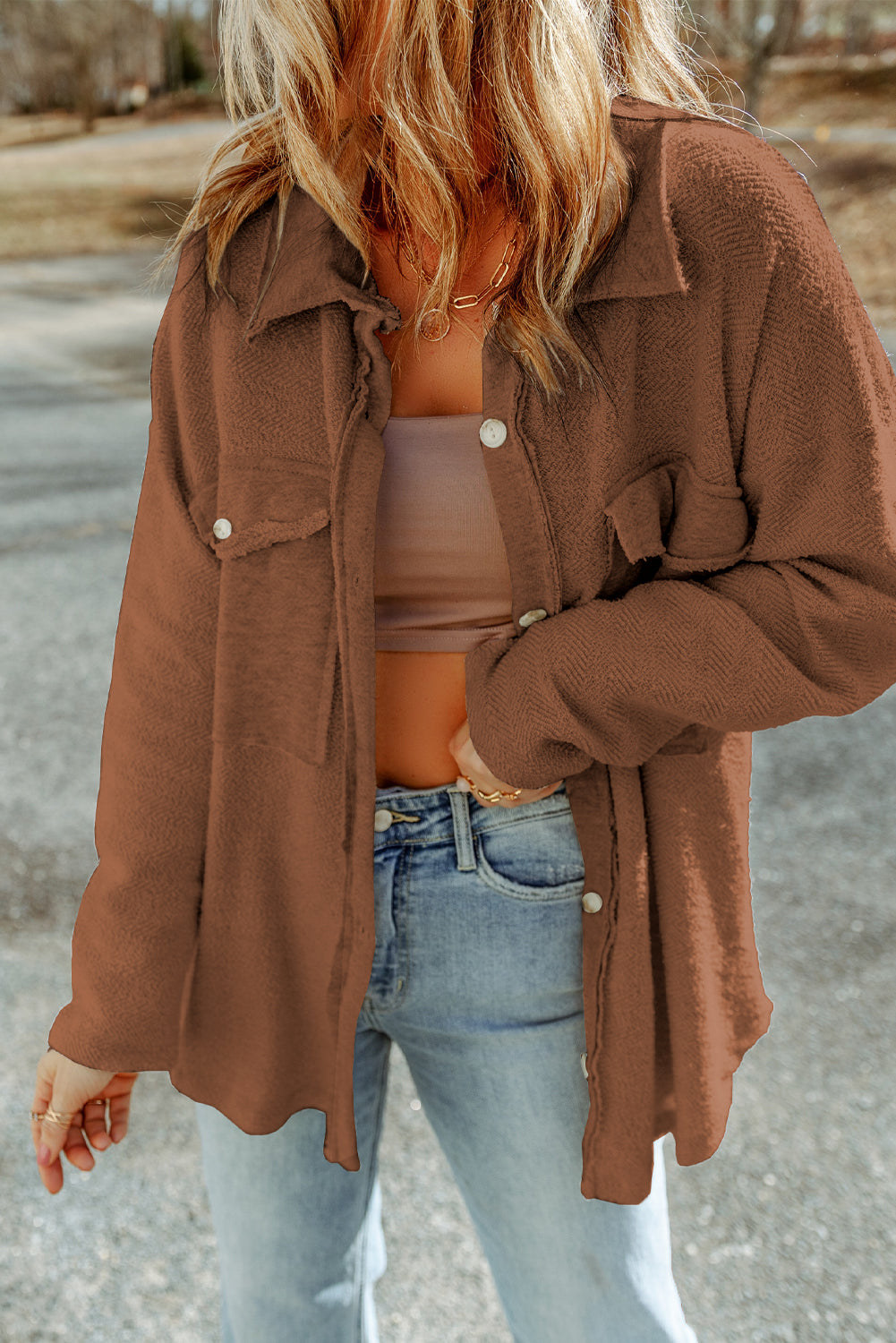 Person wearing a brown jacket, beige top, and blue jeans outdoors.