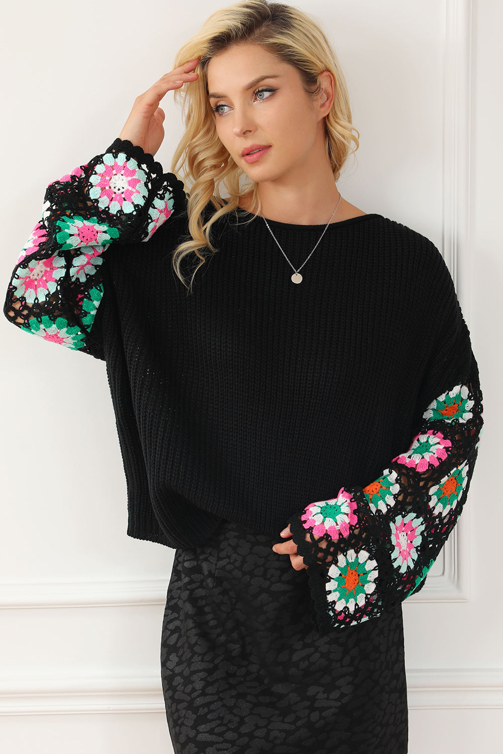 Woman wearing a black sweater with colorful floral patterns on the sleeves against a white wall.