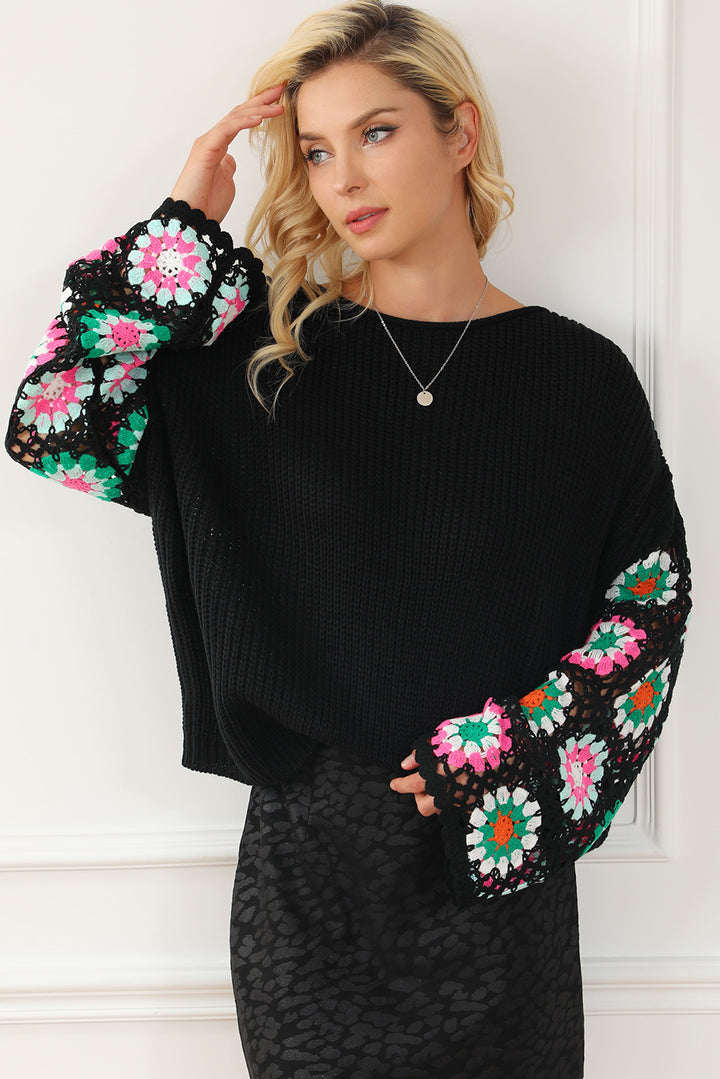 Woman wearing a black sweater with colorful floral patterns on the sleeves against a white wall.