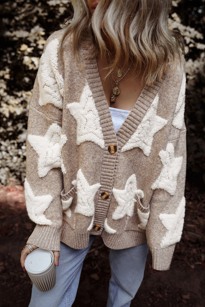 Person wearing a beige cardigan with white star patterns, holding a mug in a natural setting.