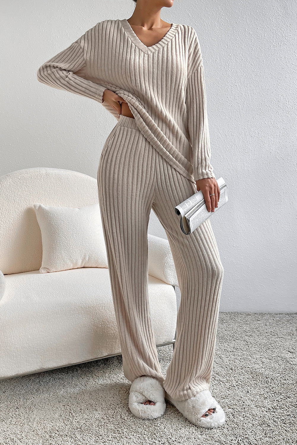 Person wearing a beige ribbed lounge set with matching slippers in a cozy living room.