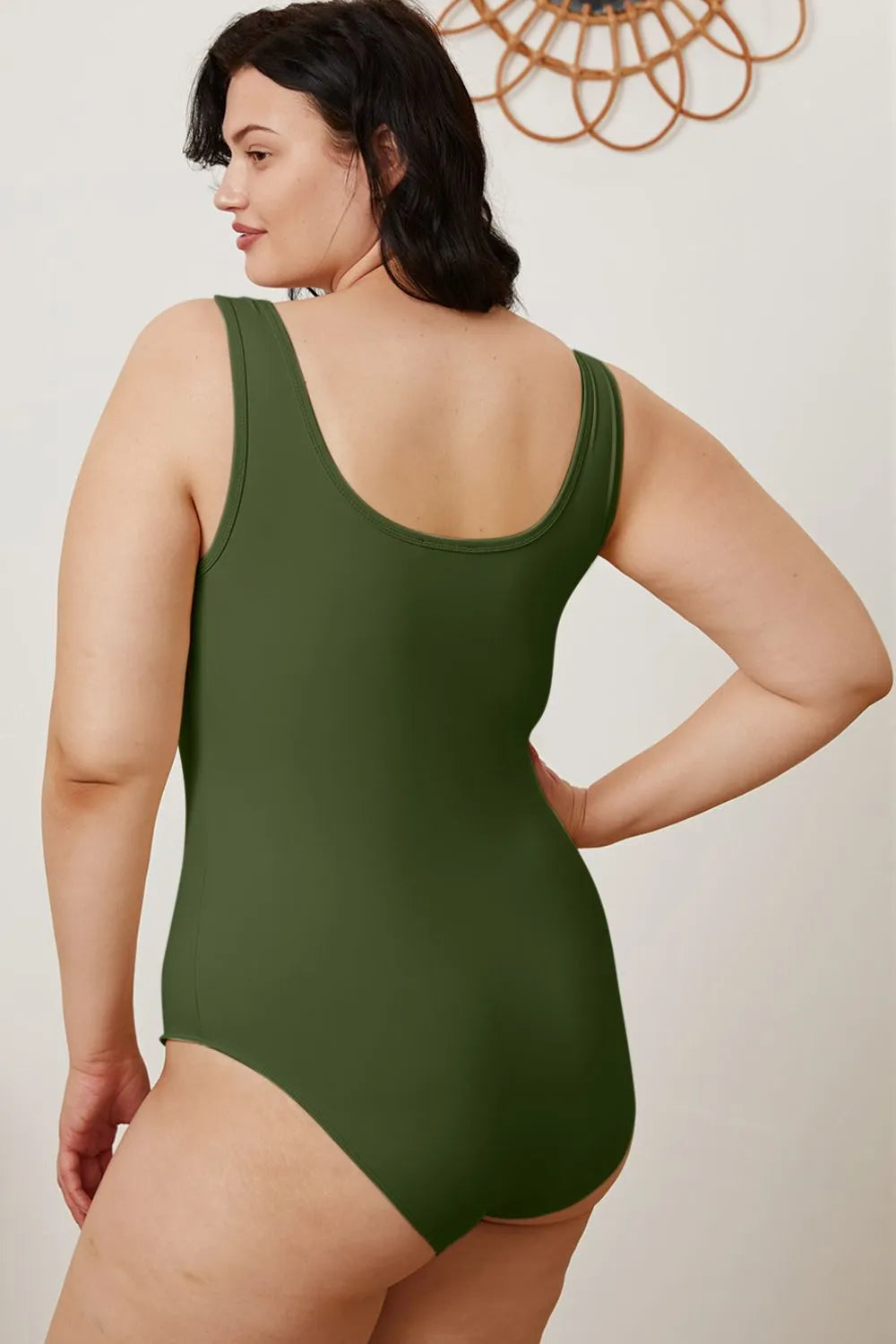 Woman wearing a green one-piece swimsuit against a plain background
