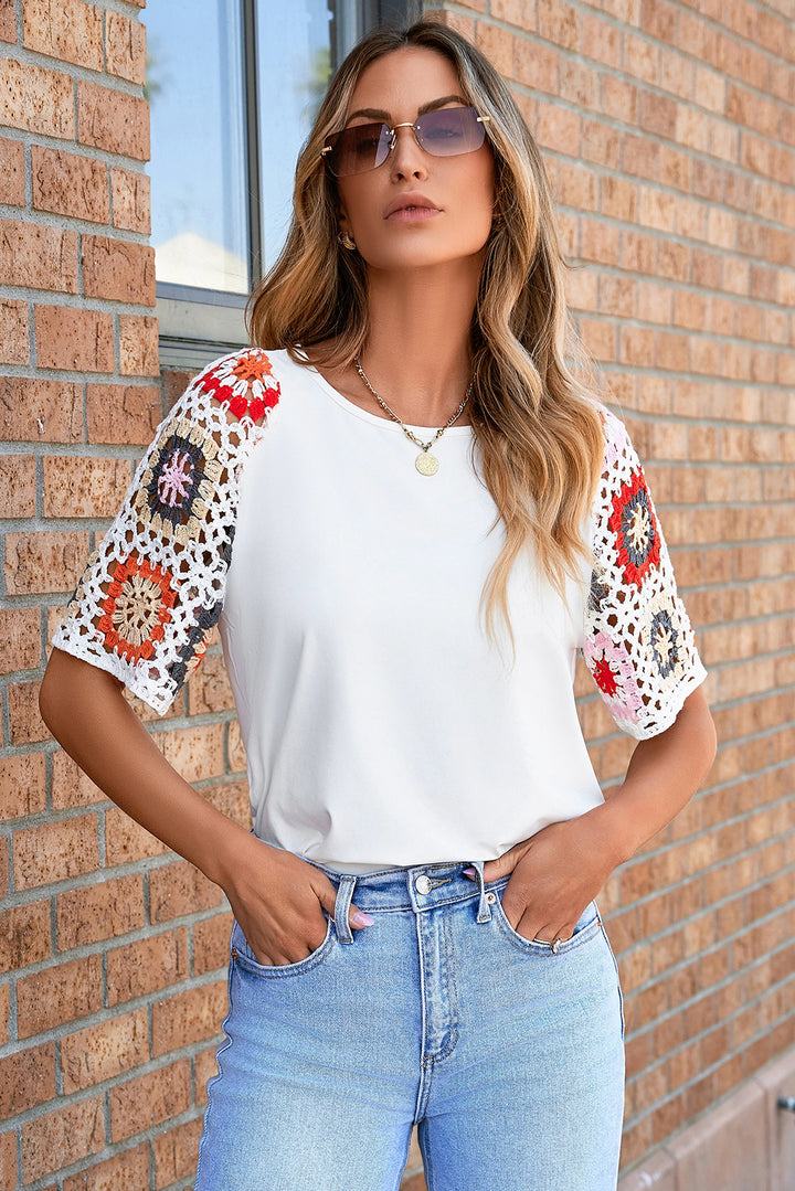 Woman wearing a white top with colorful sleeves and blue jeans against a brick wall.