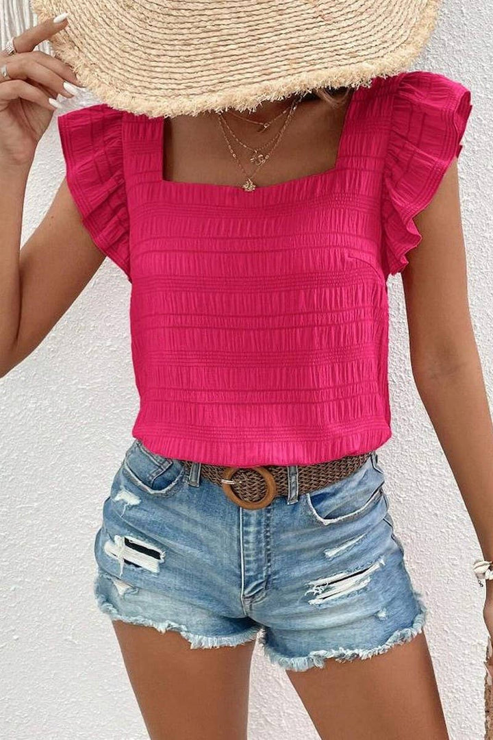 Woman wearing a rose-colored top with ruffled sleeves and square neckline and a pair of jean shorts