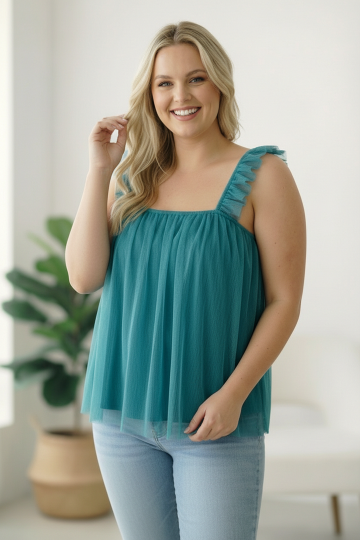 Woman wearing a teal top with ruffled straps in a bright room.