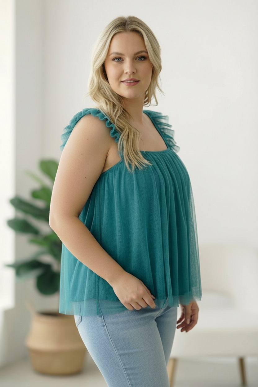 Woman wearing a teal top with ruffled shoulders in a bright room.