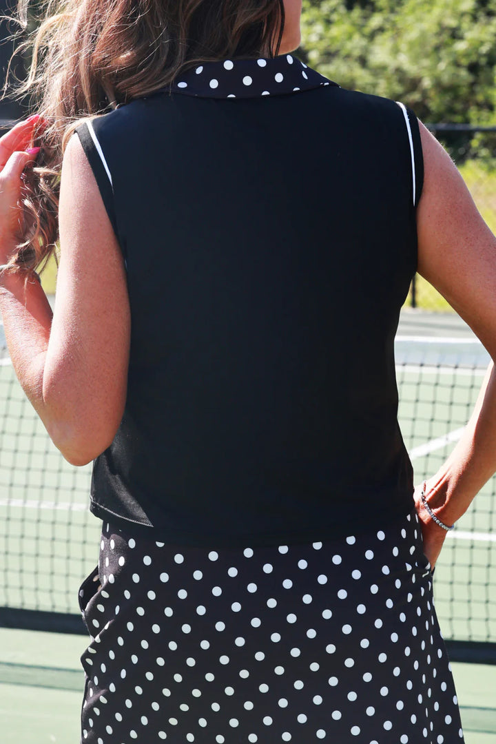 Person wearing a black sleeveless top with white polka dots and a matching skirt on a tennis court.