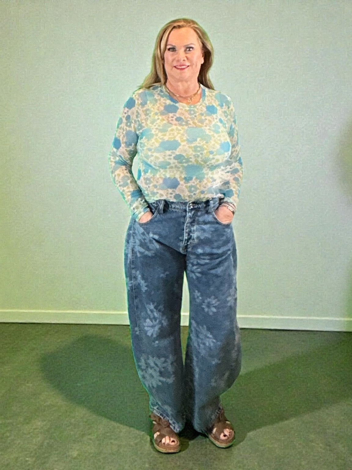 Person wearing a patterned shirt and blue jeans against a plain background