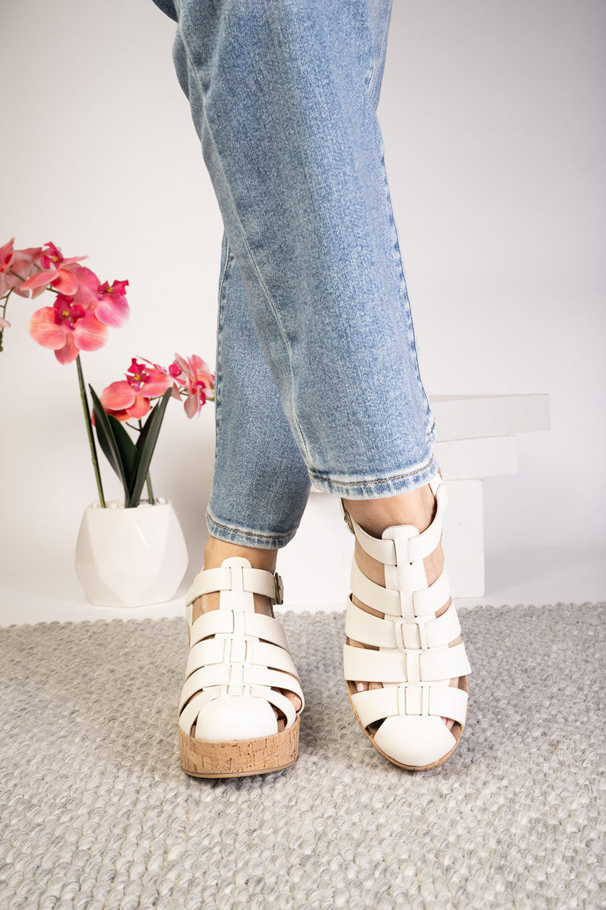 Person wearing white sandals with cork soles on a neutral background