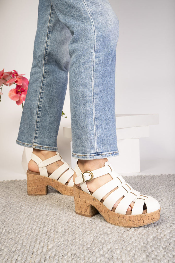 White sandals with cork soles worn with blue jeans on a neutral background
