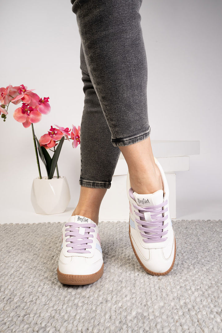 Person wearing white sneakers with purple laces on a neutral background