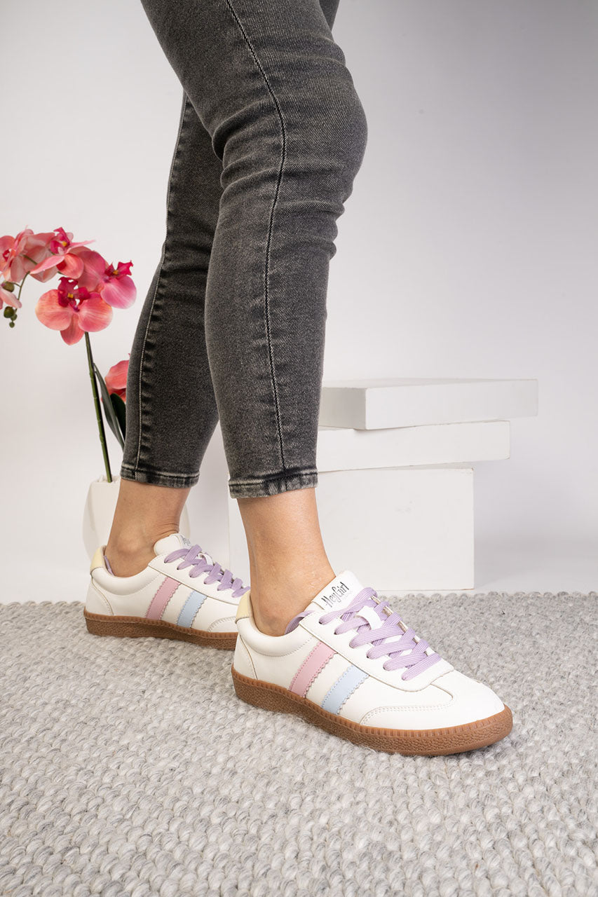 White sneakers with colorful accents worn with black jeans on a light gray floor.